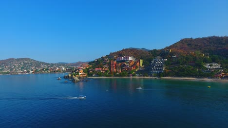 aerial video flying by the gorgeous shoreline filled with boats, white sand beaches, and the beautiful city of zihuatanejo, mexico