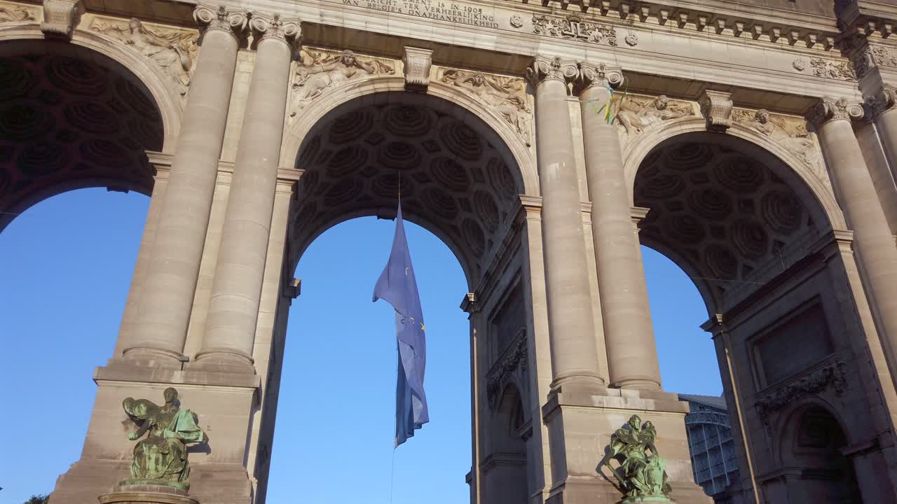 EU flag beneath Cinquantenaire arch with kite flying overhead in slow motion