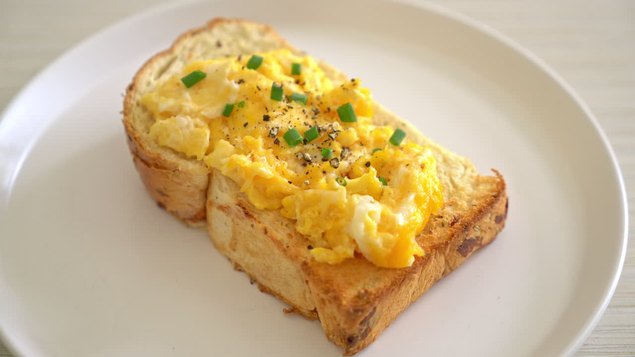 Tostadas de pan con huevos revueltos en la placa blanca.