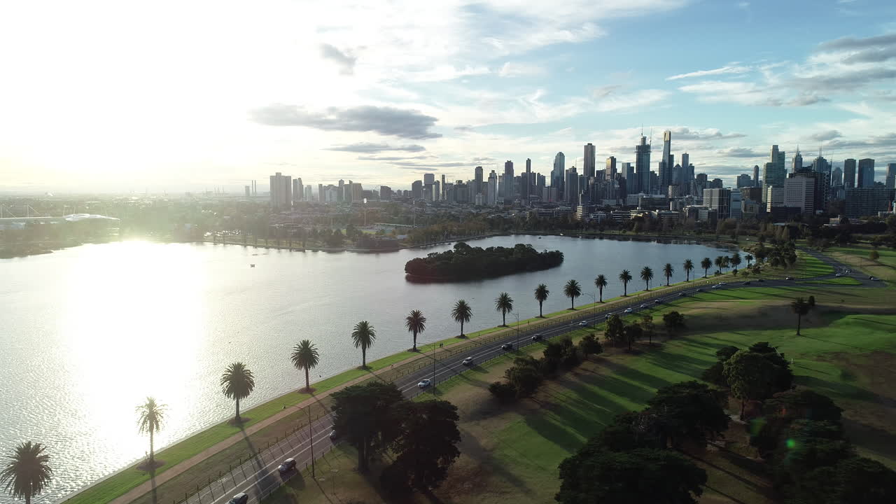 Avvicinamento aereo fluido al centro di Melbourne, con il traffico che lascia la città in fila indiana lungo il lago Albert Park.