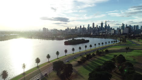 smooth aerial approach toward melbourne cbd while traffic leaves the city area in a single file beside albert park lake