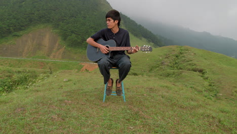 musician playing guitar and singing while sitting on hill