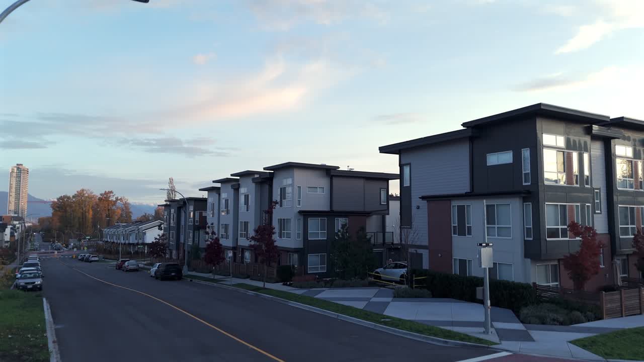 カナダ、ラングリー市、カーヴォルト - 静かな郊外の通りに、柔らかな夕空の下、遠くの山々を背景にモダンなタウンハウスが立ち並ぶ - 空撮による下降ショット