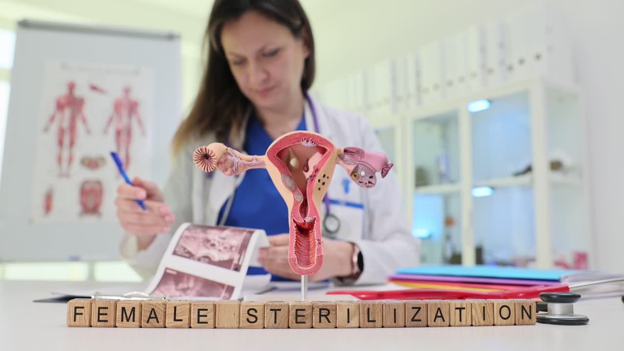Il medico spiega la sterilizzazione femminile vicino a un modello di utero e scansioni.