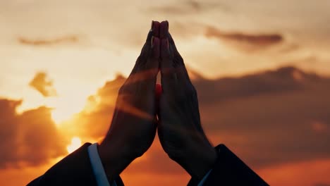 businessman silhouetted against a vibrant sunset, hands joined in prayer, embodies faith and inspiration in a serene moment