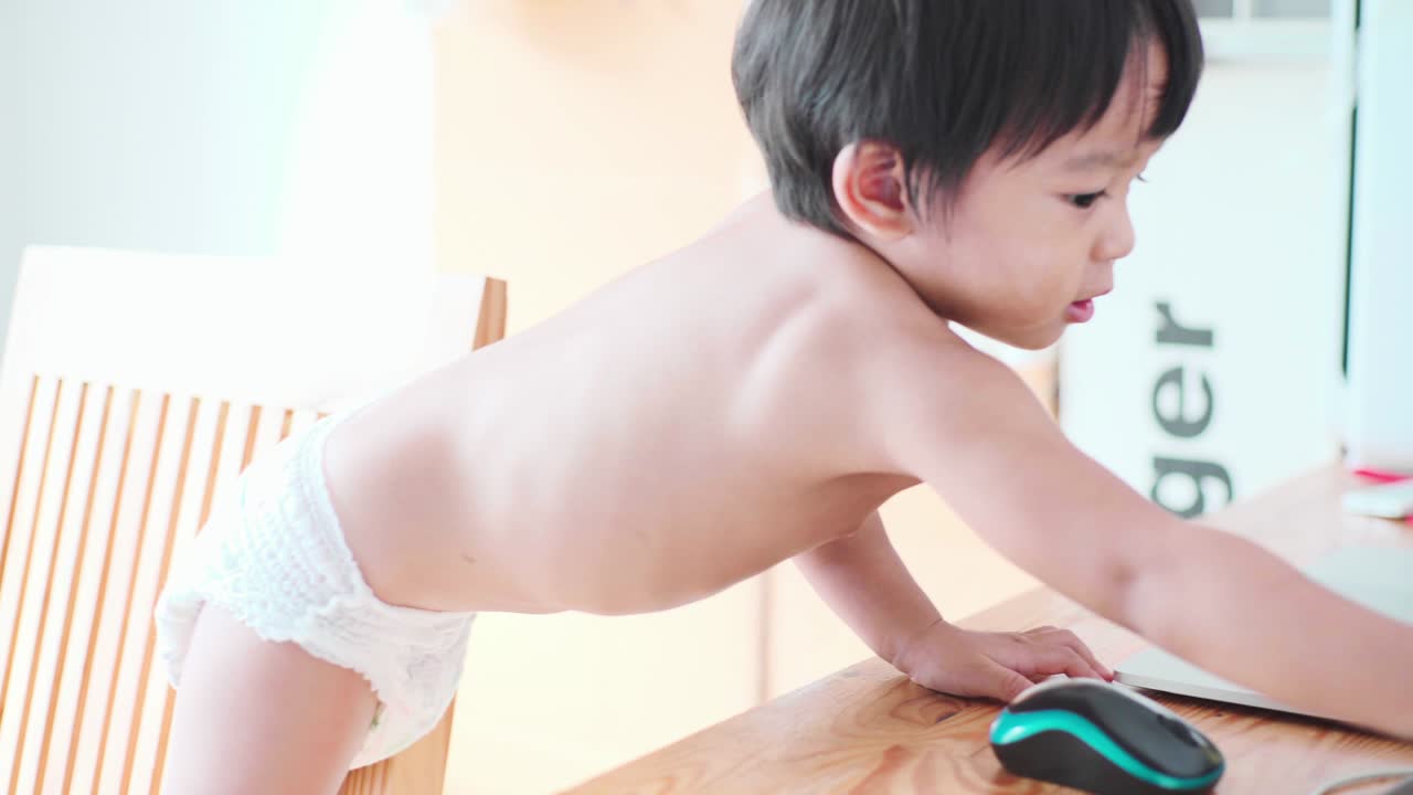 사랑스러운 유아 소년은 노트북 컴퓨터를 재생하기 위해 테이블에 crawling