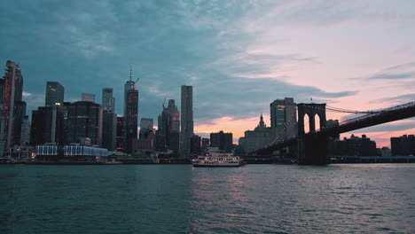 Vista-Crepuscular-Sobre-Nueva-York-Y-El-Puente-De-Brooklyn-Que-Cruza-El-Río-Este,-Viaje-En-Ferry