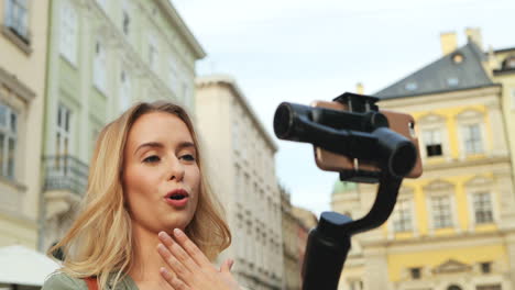 Close-up-view-of-caucasian-blonde-young-woman-recording-a-video-on-the-smartphone-while-holding-it-with-a-selfie-stick-in-the-street