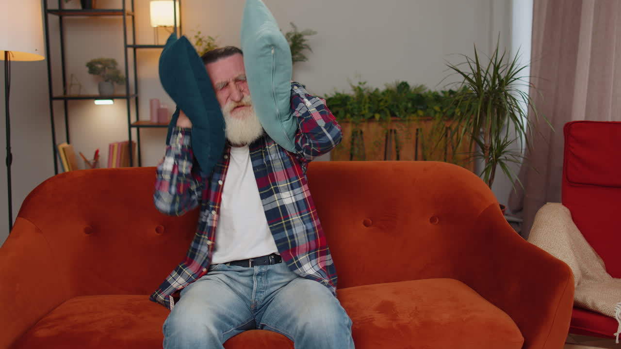 Repair work at neighbours concept, irritated man at home cover ears with pillows annoyed by noise