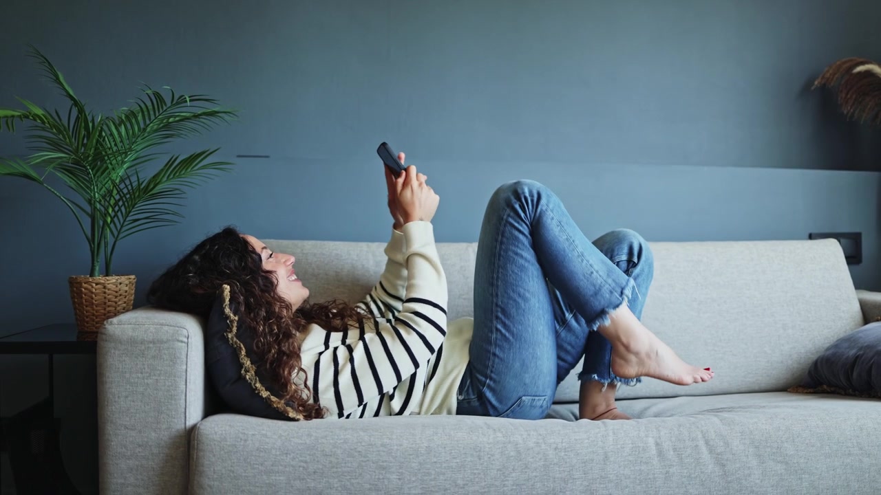 Mujer joven relajándose en el sofá y usando su smartphone