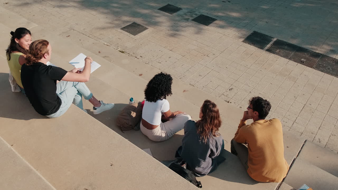 The group of happy students with study items is sitting on the stairs. Top view