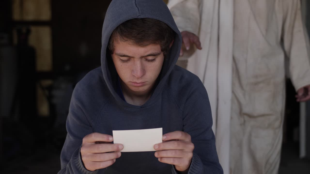 흰색의 너덜너덜한 옷을 입은 예수가 어린 십대 소년 뒤에 서 있다