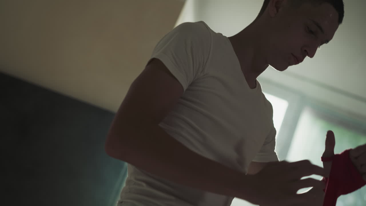 Fighter uses hand wrap for boxing in combat gym. Concentrated athlete applies protective supply for palms in martial arts club slow motion. Sportive life
