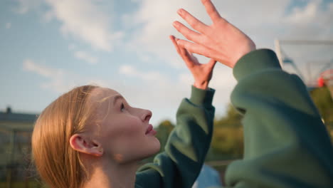 close-up of athlete in green sweater playing volleyball, with another lady in blue sweater blurred in the background, a building is visible in the distance with clear sky