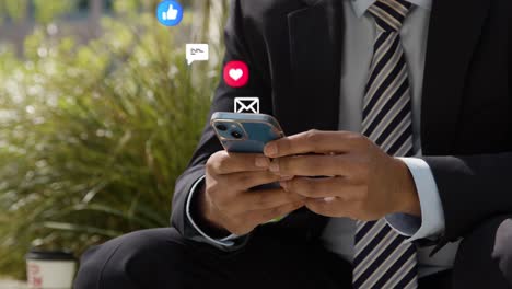 close up de un hombre de negocios sentado fuera de las oficinas de la ciudad mirando un teléfono móvil con emojis de gráficos en movimiento que muestran múltiples mensajes y notificaciones de redes sociales