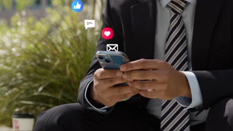 close up of businessman sitting outside city offices looking at mobile phone with motion graphics emojis showing multiple messaging and social media notifications