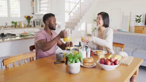 pareja feliz y diversa sentada a la mesa y desayunando