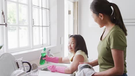 video of happy biracial mother and daughter cleaning kitchen