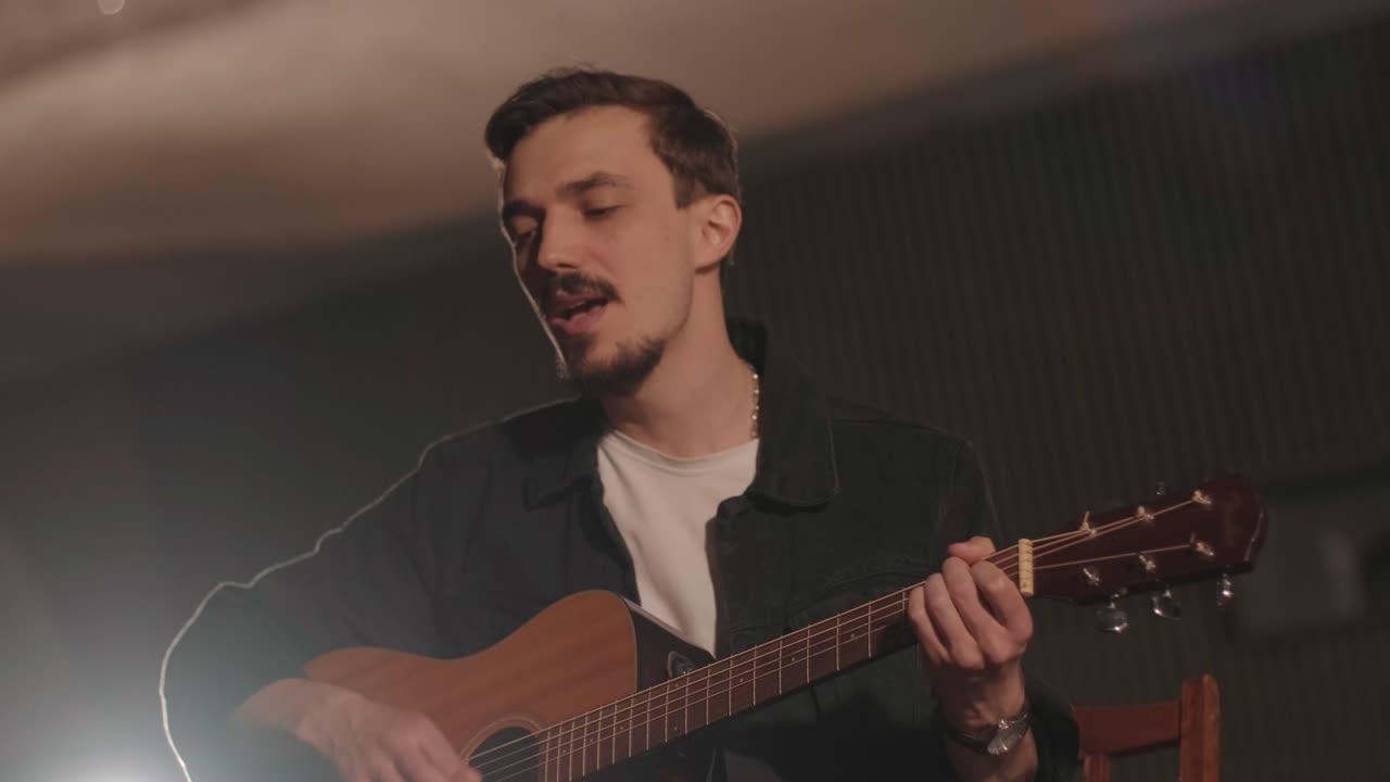 un chico guapo toca una guitarra acústica en un cine abandonado. el músico canta una canción y acompaña en la guitarra