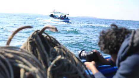 a man shooting a video of the boat in front of him while at sea in the daytime