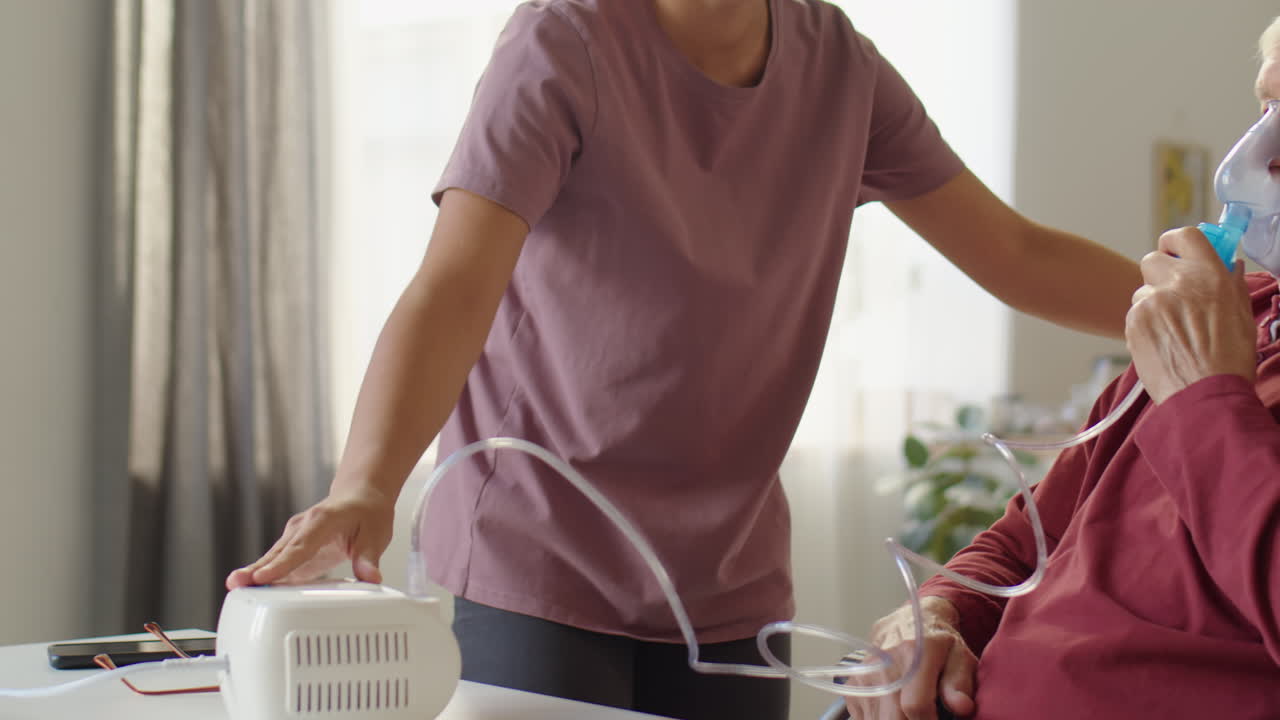 Caregiver Assisting elderly Man with Nebulizing at Home