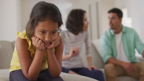 triste chica hispana sentada en el sofá con los padres discutiendo en el fondo