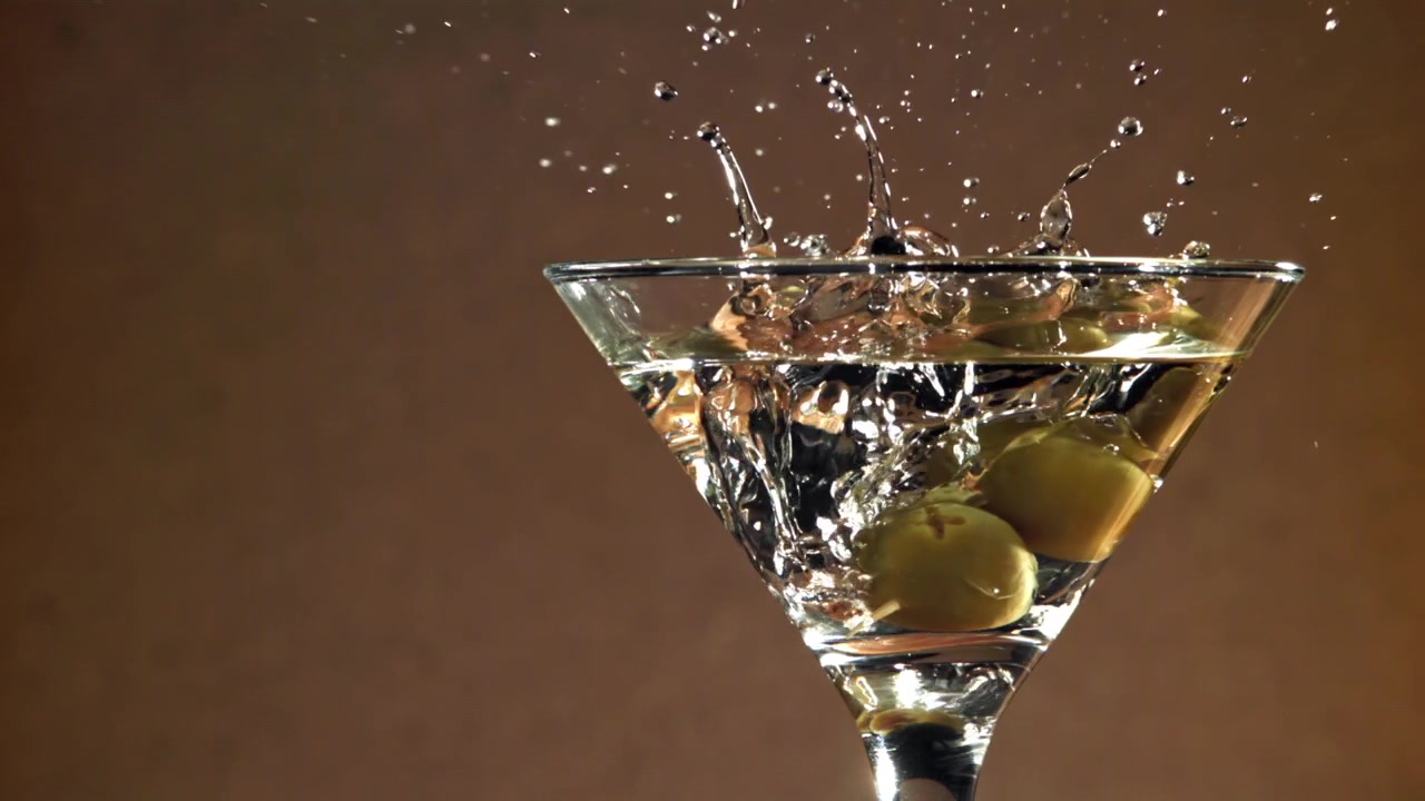 Olive verdi che cadono in un bicchiere da Martini al rallentatore.
