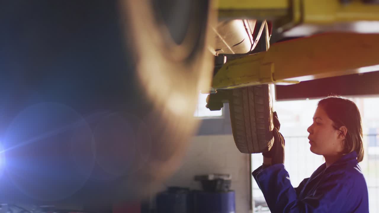 Animation of asian mid adult female mechanic standing under car examining tires in auto repair shop