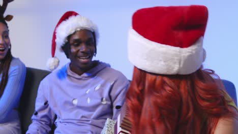 fotografía de estudio de amigos de la generación z dando regalos de navidad sentados en el sofá con sombrero de papá noel y cuernos de reno 2