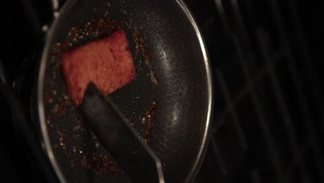 cooking spam meat in stainless steel pan, close-up vertical