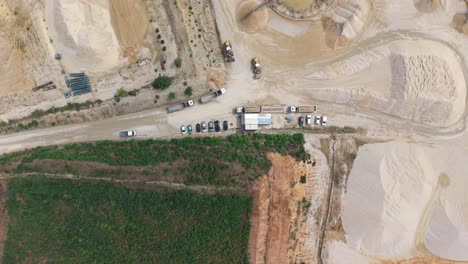 top-down aerial view of an active sand mining site with trucks lined up, excavators operating, and several parked vehicles near a small control facility