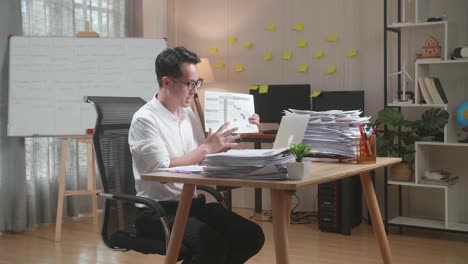 hombre asiático con documentos que explican el trabajo en papel mientras tiene una llamada de video en una computadora portátil en la oficina