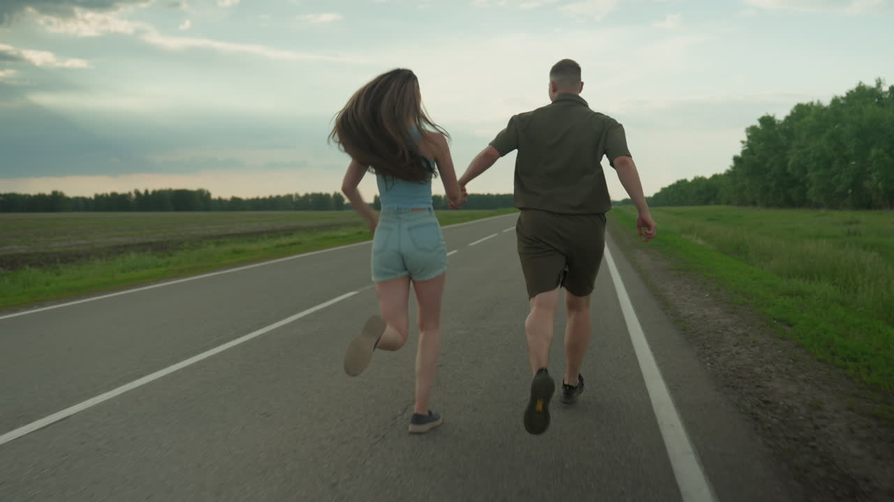 back view of siblings running hand in hand along country road with distant truck approaching down asphalt highway under moody sky capturing energetic moment of carefree journey