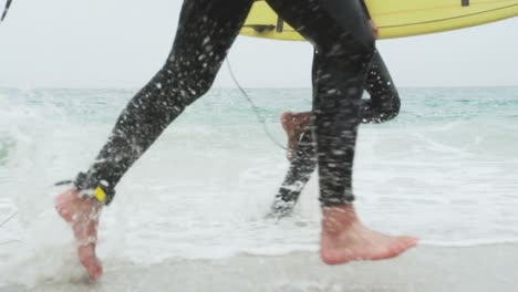 sección baja de dos surfistas masculinos corriendo con tabla de surf en la playa 4k