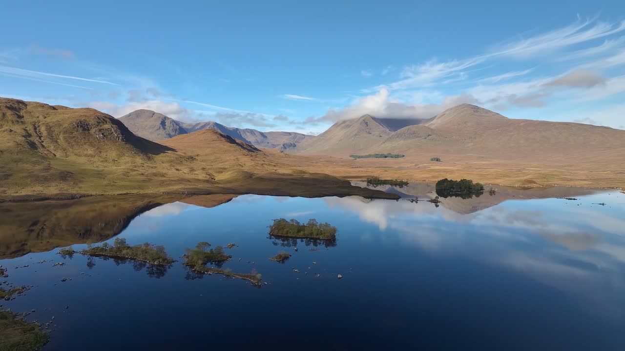 Mirror calm dark water reflecting mountain peaks and wispy clouds at Lochan na h-Achlaise, Rannoch Moor, Glencoe.