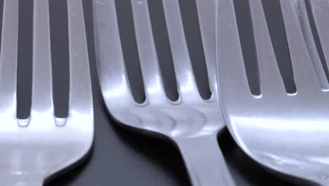 very close shot of four steel forks on a black bacground, rotating motion