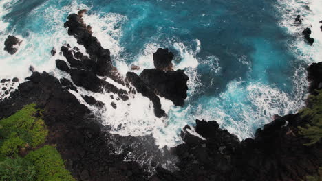 aerial view of rocky cove with waves crashing around dark rocks in hawaii