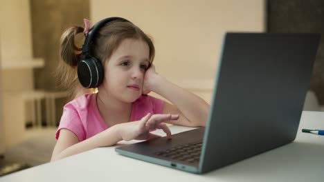 small girl wearing headphones studying online from home with distance teacher