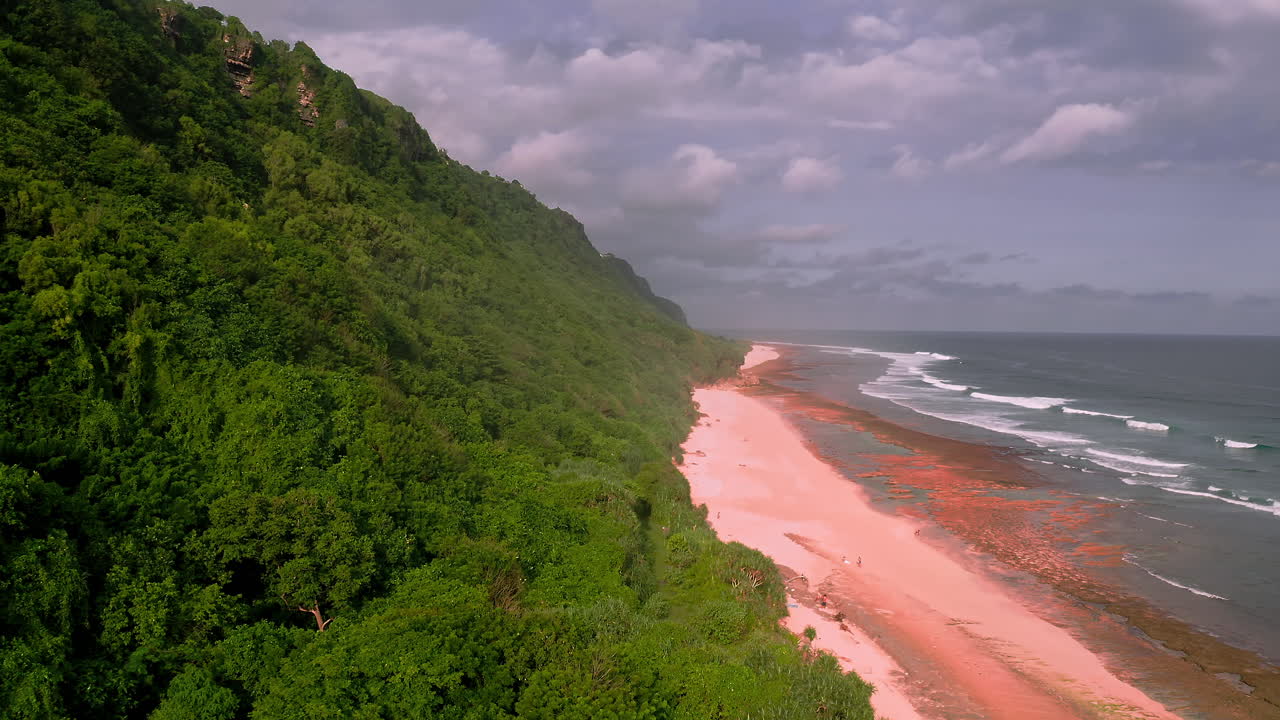 nubes y salpicaduras de mar sobre una playa de arena empinada con follaje exuberante en bali