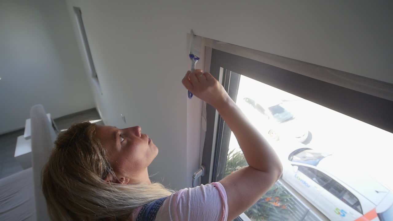 Vrouw met verfkwast schildert rond raam tijdens doe-het-zelf schilderklus vanuit hoog camerastandpunt in slow motion