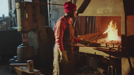 blacksmith hammering metal rod heated in forge in workshop