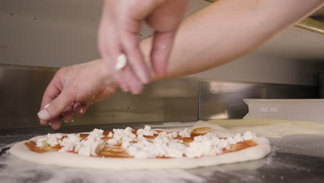 close up view of a chef hands spreading cheese on pizza dough on a restaurant kitchen countertop 1