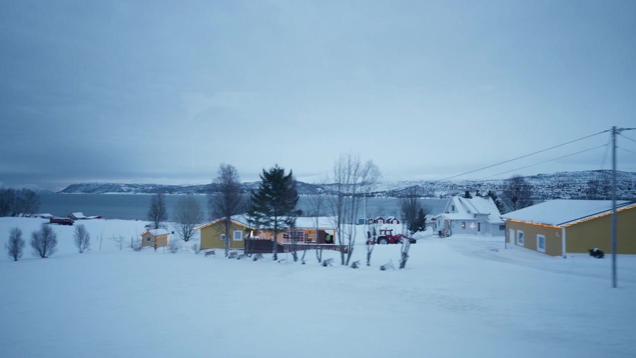 Snow covered homes beside fjord in Arctic Norway viewed from moving vehicle