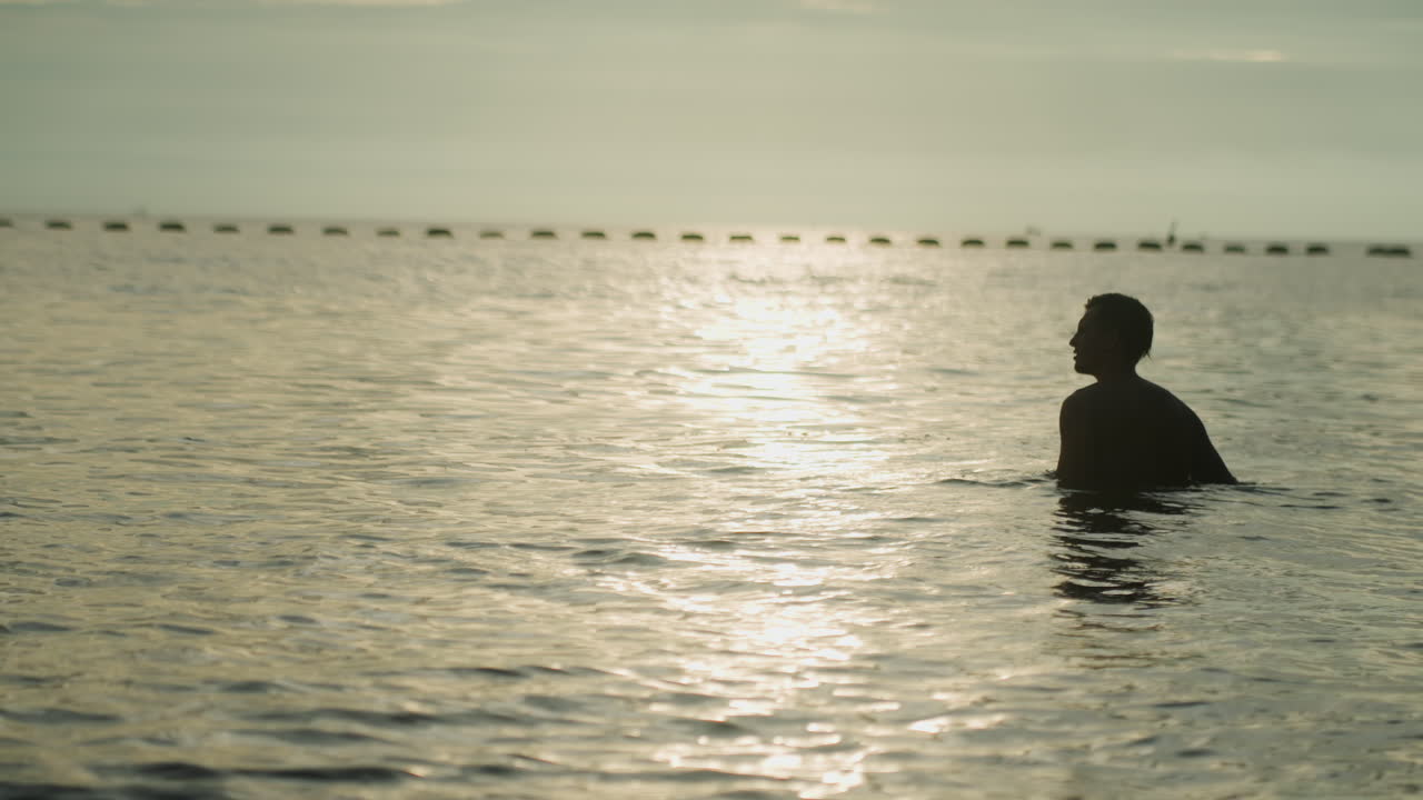 夕焼けの海に向かう男性のシルエット。腕をわずかに上げた勝利を収めたかのような姿、水面に広がる温かい輝き、地平線を背景にした逆光の輪郭。再生を示唆する、活気に満ちながらも穏やかな雰囲気。
