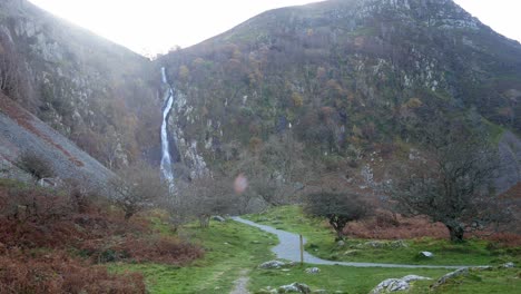 Autumn-nature-trail-leading-to-cascading-waterfall-through-bare-leafless-trees-with-blowing-leaves