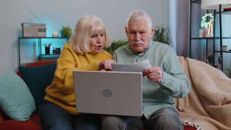 stressed senior family couple man woman discuss unpaid bank debt holding bills throws paper at home