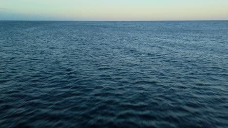 aerial dolly, dark ocean water at sunset with golden glow hues on horizon