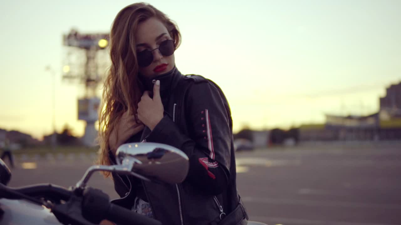 Portrait of a female biker in leather jacket and shorts sitting on her bike and holding a handlebar. Close up of young sexy