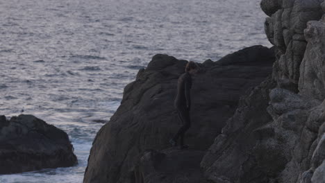 adult male climbs cliff and cliff jumps off into the ocean at sunset