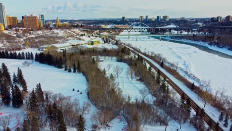 aerial winter flyover drop at victoria park manmade quiet ice rink connected to an infinity skate track next to forest road snow covered north saskatchewan river by royal glenora club downtown city3-4